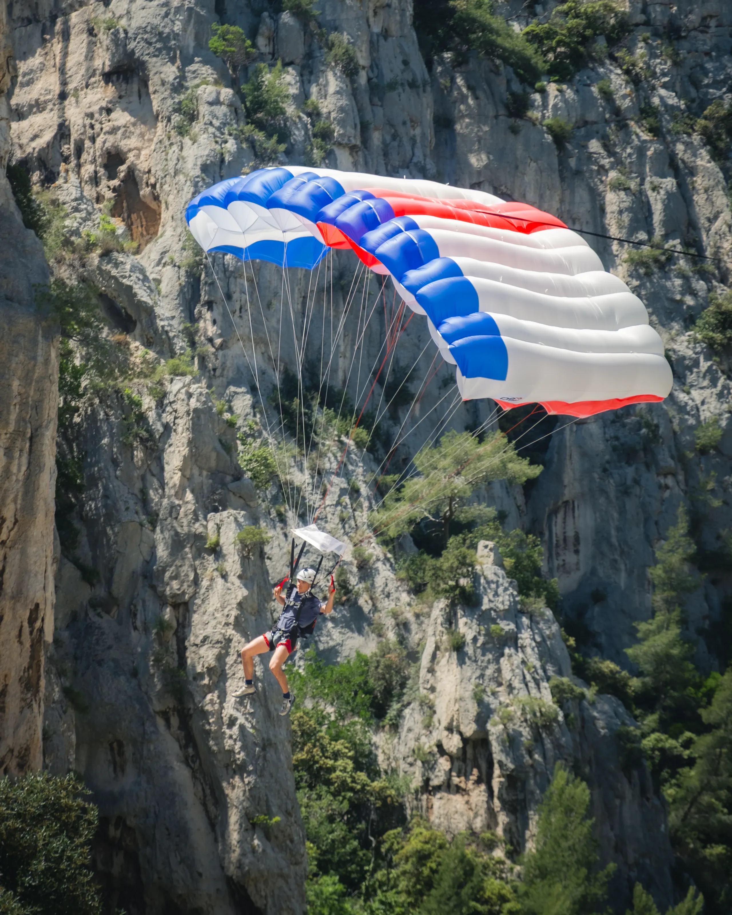 A base jumper with a red, white and blue wing flying past limestone cliffs