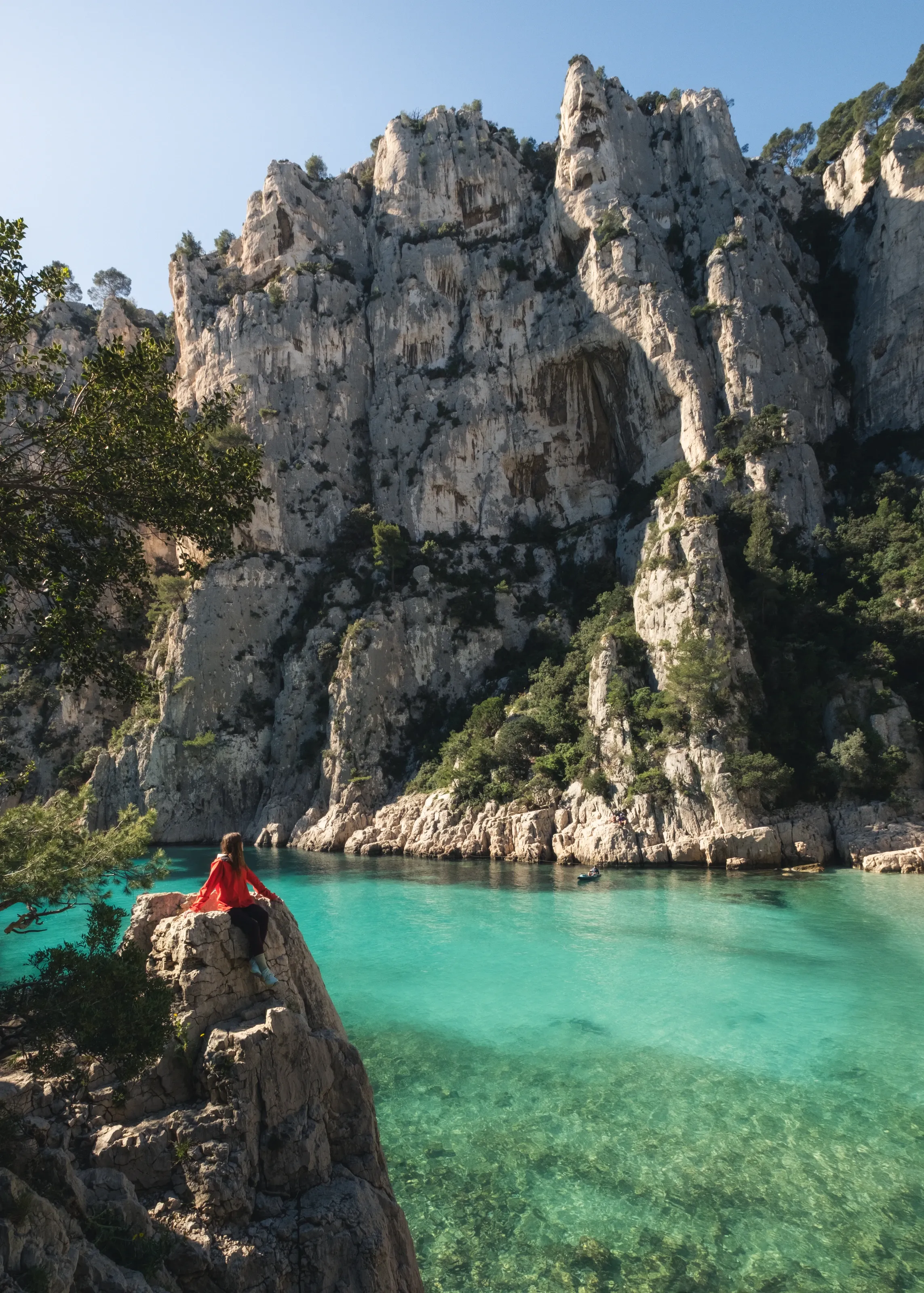 Marina in a red jacket on a rock above a turquoise cove below white cliffs