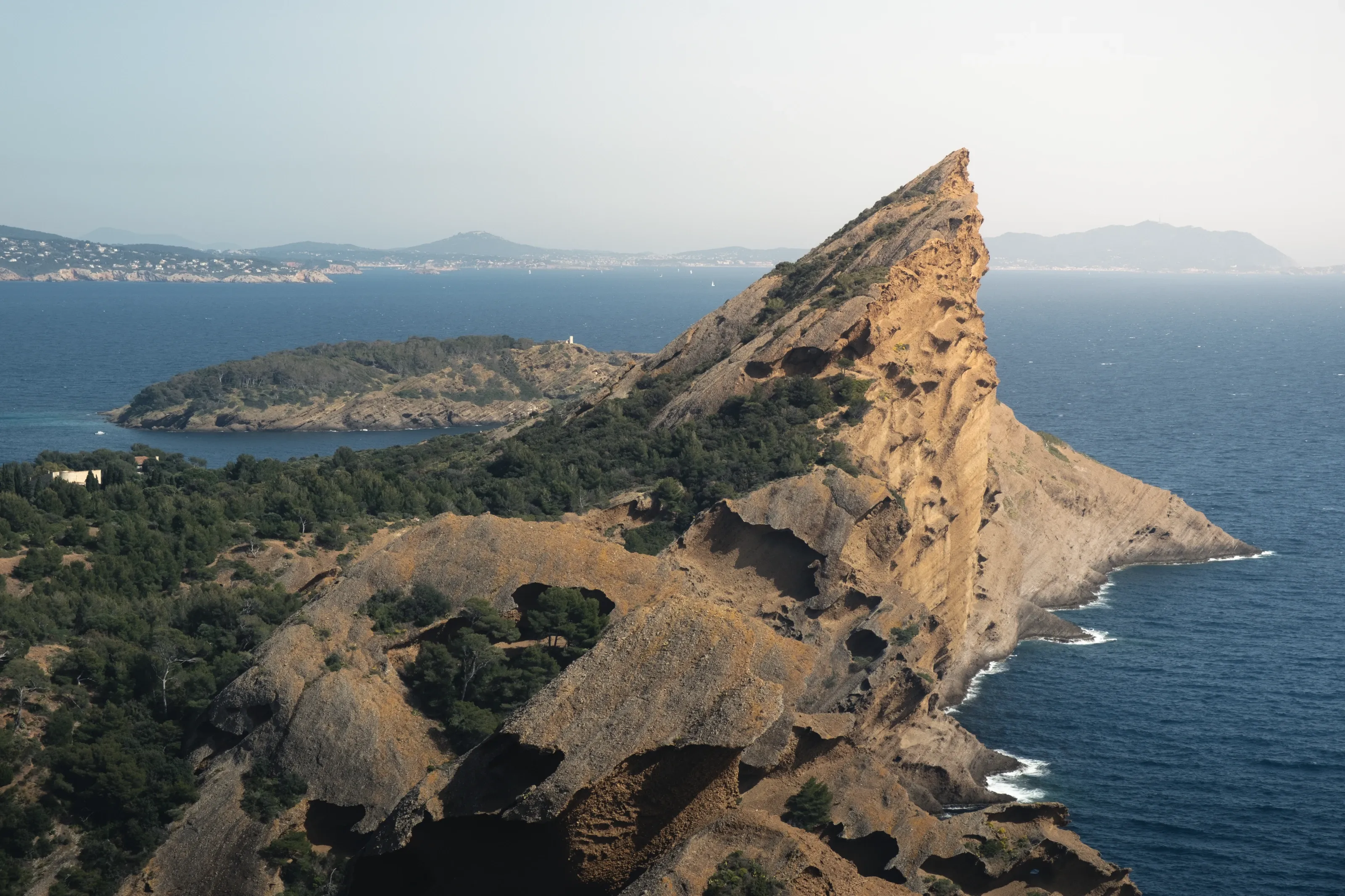 A sharp ochre ridge above the sea, the coast in haze behind it